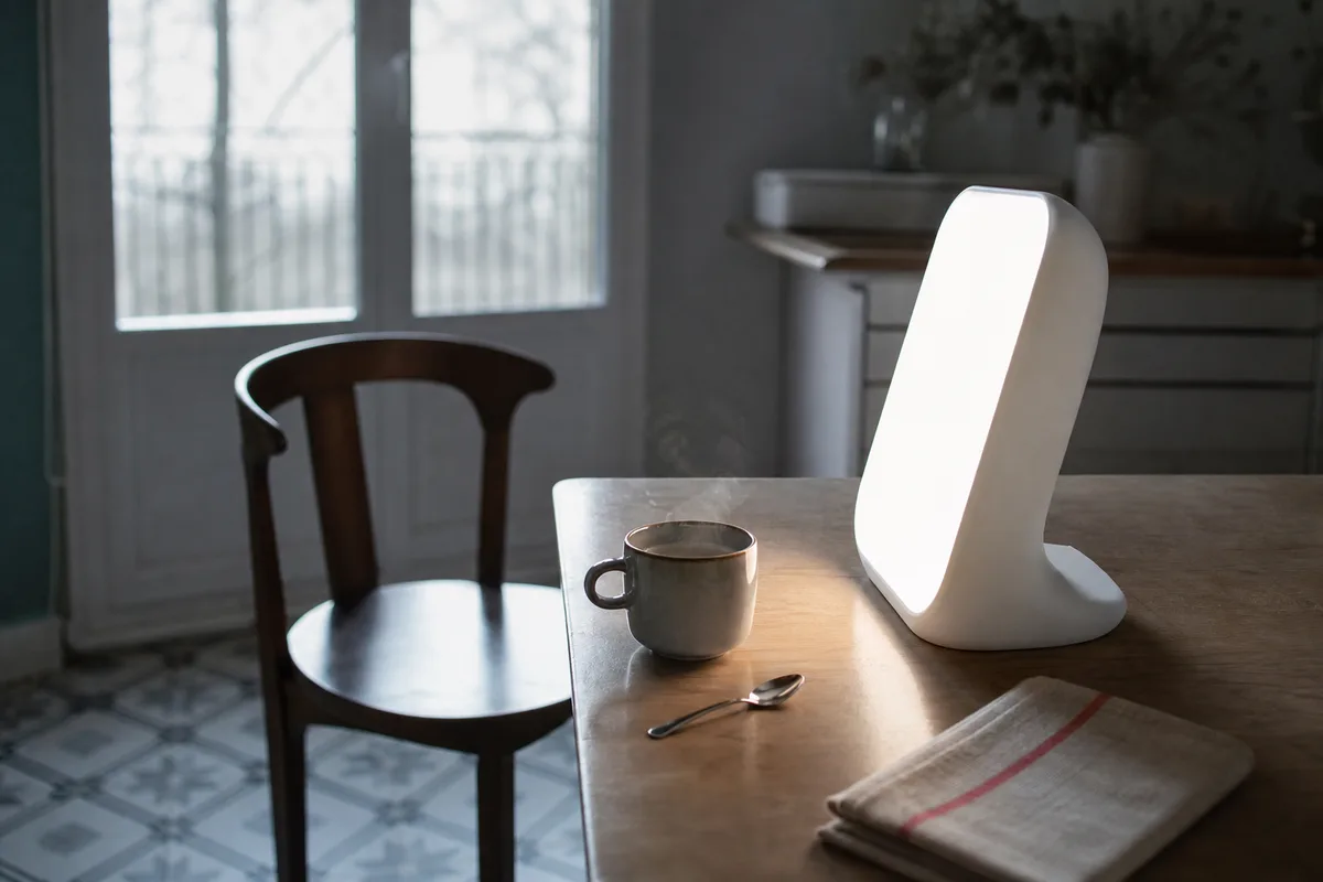 Lampe de luminothérapie posée sur une table de petit-déjeuner près d&rsquo;une fenêtre au petit matin